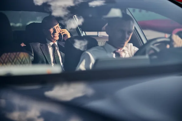 A professional driver and a passenger in a suit are seated inside a luxury car.
