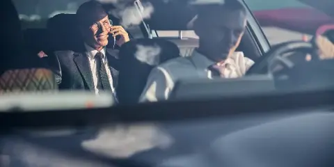 A professional driver and a passenger in a suit are seated inside a luxury car.