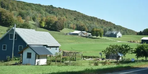 Rural landscape with a blue house and green fields near a road in Cattaraugus, NY
