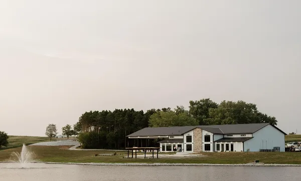 Exterior view of the Gathering Grounds estate building situated on a large lawn next to a lake with a fountain.