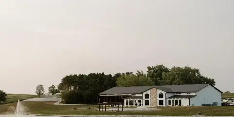 Exterior view of the Gathering Grounds estate building situated on a large lawn next to a lake with a fountain.