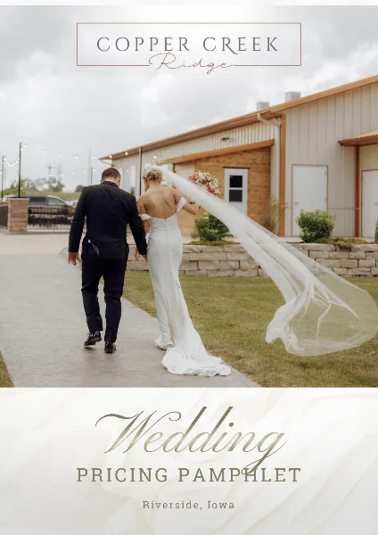 A bride and groom walking away from the camera in front of the Copper Creek Ridge venue building.