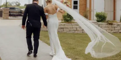 A bride and groom walking away from the camera in front of the Copper Creek Ridge venue building.