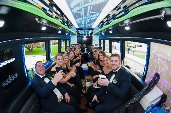 A group of people in formal wear celebrating inside a party bus with green and blue LED lighting.