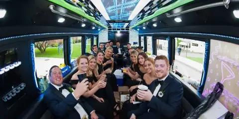 A group of people in formal wear celebrating inside a party bus with green and blue LED lighting.