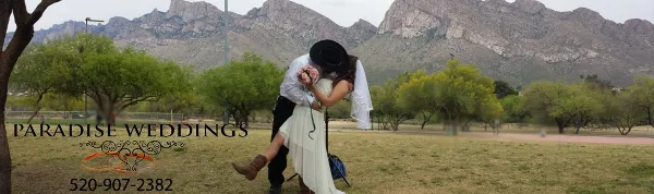 A bride and groom kissing outdoors in a park with a mountain range in the background.