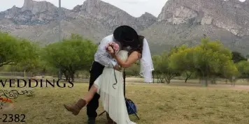 A bride and groom kissing outdoors in a park with a mountain range in the background.