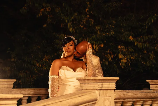 A bride and groom share an intimate moment on a stone balcony at night, with the groom kissing the bride's forehead.