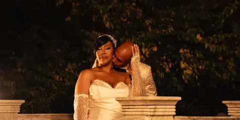 A bride and groom share an intimate moment on a stone balcony at night, with the groom kissing the bride's forehead.