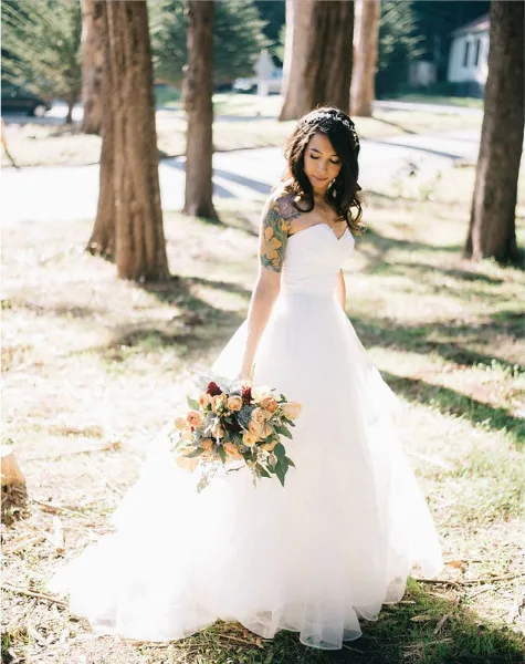 A bride in a white gown with styled hair and makeup holding a bouquet outdoors.