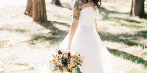 A bride in a white gown with styled hair and makeup holding a bouquet outdoors.