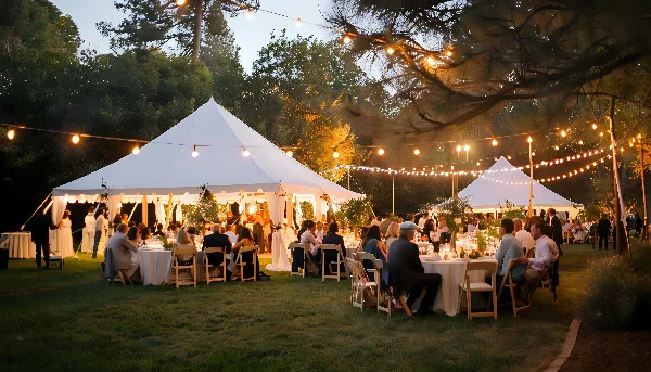 An outdoor event setup featuring a large white tent, tables, and chairs with string lights.