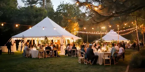 An outdoor event setup featuring a large white tent, tables, and chairs with string lights.