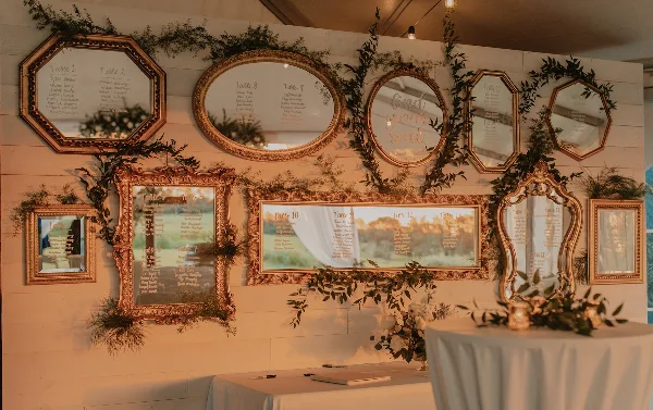A decorative event seating chart made of framed mirrors and greenery on a white wall.