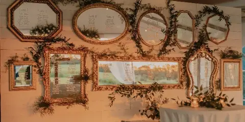 A decorative event seating chart made of framed mirrors and greenery on a white wall.