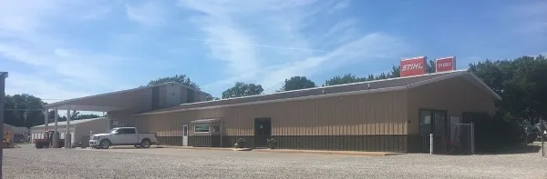 Exterior view of a commercial equipment rental center with a gravel lot and a pickup truck parked in front.