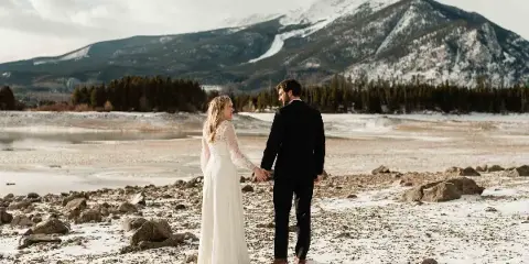 A bride and groom holding hands in a snowy landscape with mountains in the background.
