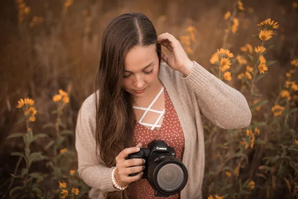 A woman holding a Canon camera in a field of yellow flowers.