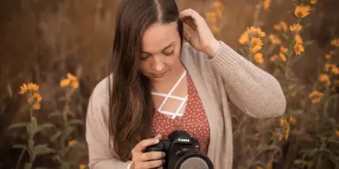 A woman holding a Canon camera in a field of yellow flowers.