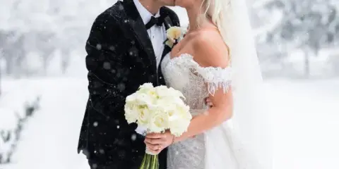 A bride and groom sharing a kiss in a snowy landscape, with the bride holding a white bouquet.