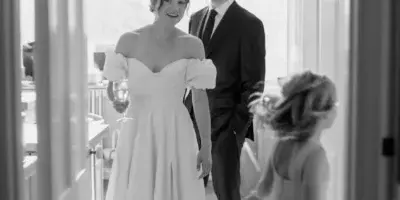 A black and white photograph of a bride and groom standing in a doorway, with a young girl in the foreground.