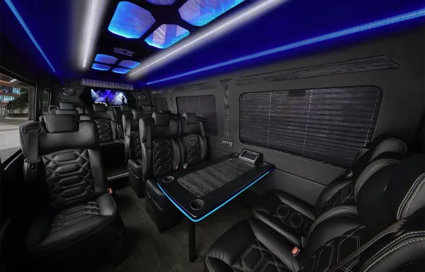 Interior of a luxury Sprinter limousine with black leather seats, a center table, and blue LED lighting.