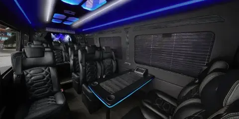 Interior of a luxury Sprinter limousine with black leather seats, a center table, and blue LED lighting.