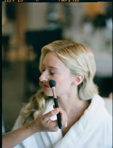 A makeup artist applying makeup to a bride's face with a brush.