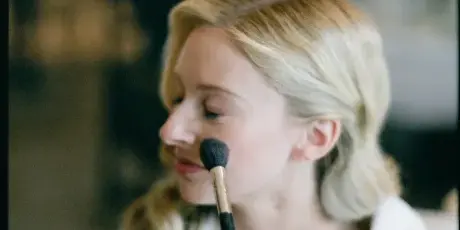 A makeup artist applying makeup to a bride's face with a brush.