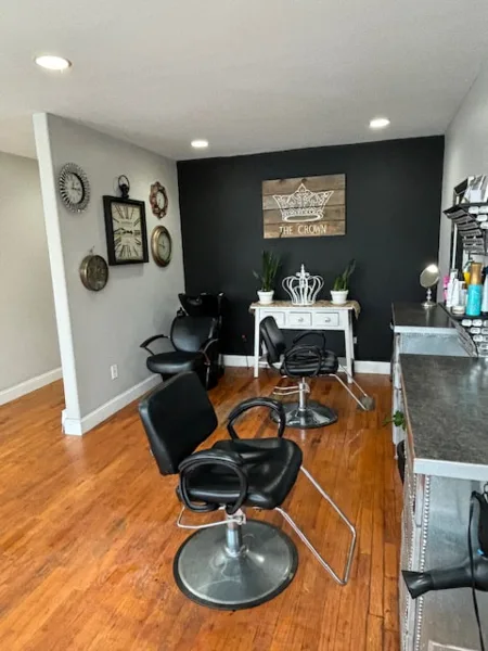 Interior view of a hair and makeup salon with black styling chairs, a wooden sign reading 'The Crown,' and a vanity area.