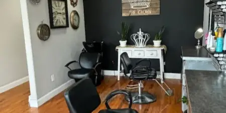 Interior view of a hair and makeup salon with black styling chairs, a wooden sign reading 'The Crown,' and a vanity area.