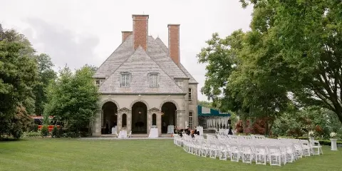 An outdoor wedding ceremony setup with rows of white chairs on a lawn in front of a historic stone building.
