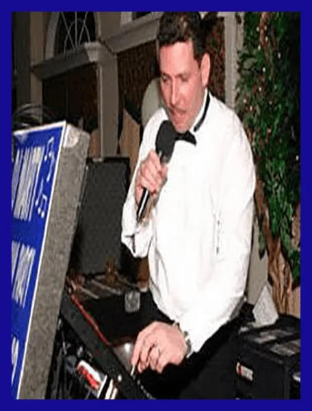 A professional DJ in a white shirt and bow tie emceeing an event while operating a sound console.