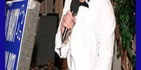 A professional DJ in a white shirt and bow tie emceeing an event while operating a sound console.