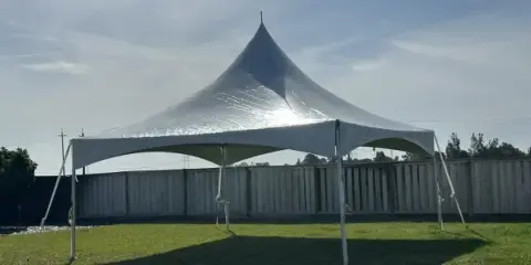 A large white event tent set up on a grassy lawn under a blue sky.