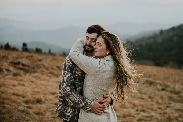 A couple embracing in a field with mountains in the background.