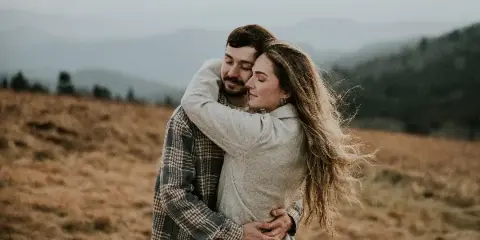 A couple embracing in a field with mountains in the background.