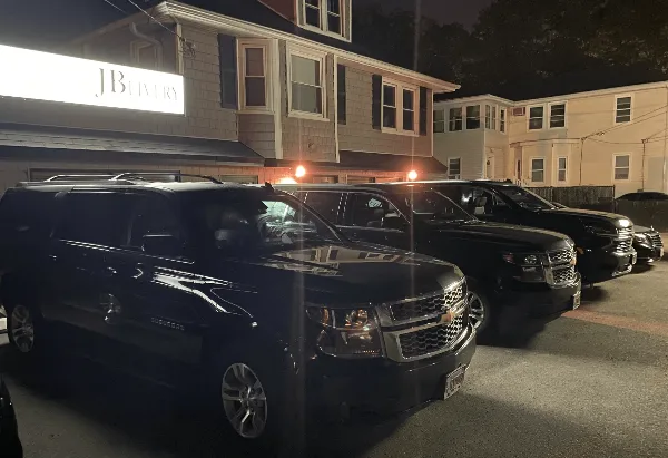 A row of black Chevrolet Suburban limousines parked outside a building with a JB Livery sign