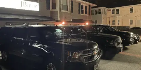 A row of black Chevrolet Suburban limousines parked outside a building with a JB Livery sign