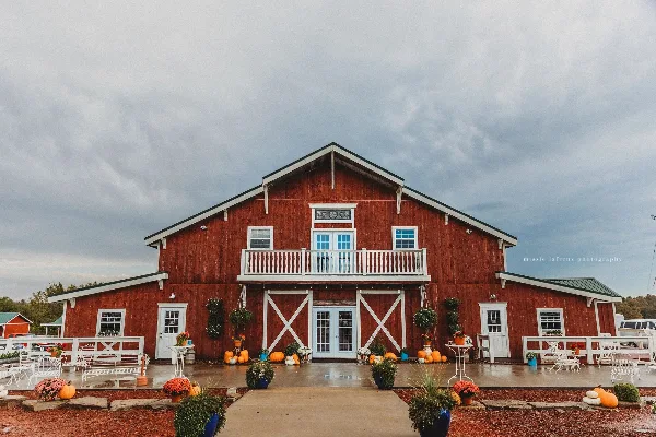 Exterior view of a large red two-story barn with white trim, a balcony, and outdoor seating area.