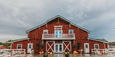 Exterior view of a large red two-story barn with white trim, a balcony, and outdoor seating area.