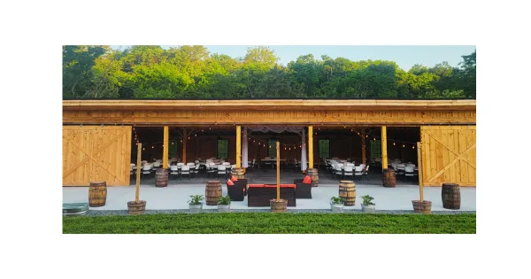 Exterior view of a modern timber frame barn venue with open-air sides, set up with white chairs and string lights for an event.