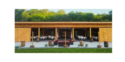 Exterior view of a modern timber frame barn venue with open-air sides, set up with white chairs and string lights for an event.