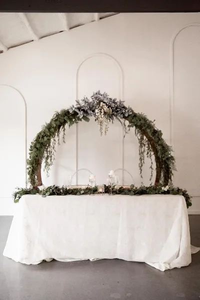 A wedding ceremony setup with a floral arch and a table decorated with candles and greenery.