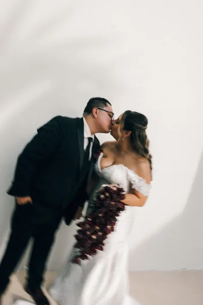 A bride and groom kissing in a white studio setting.