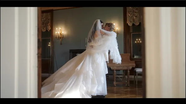 A cinematic still of a bride and groom sharing a kiss in an elegant room with a grand piano and candelabras.