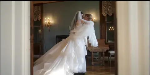 A cinematic still of a bride and groom sharing a kiss in an elegant room with a grand piano and candelabras.