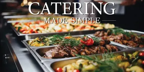A catering buffet featuring trays of grilled meat, roasted vegetables, and other prepared dishes.