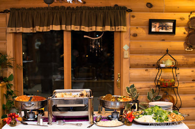 A catering buffet setup featuring multiple chafing dishes with food, set on a table in a rustic wooden venue.