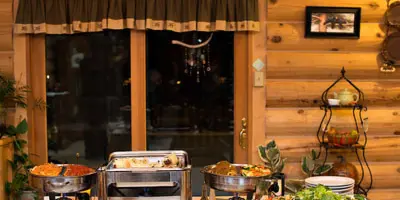 A catering buffet setup featuring multiple chafing dishes with food, set on a table in a rustic wooden venue.